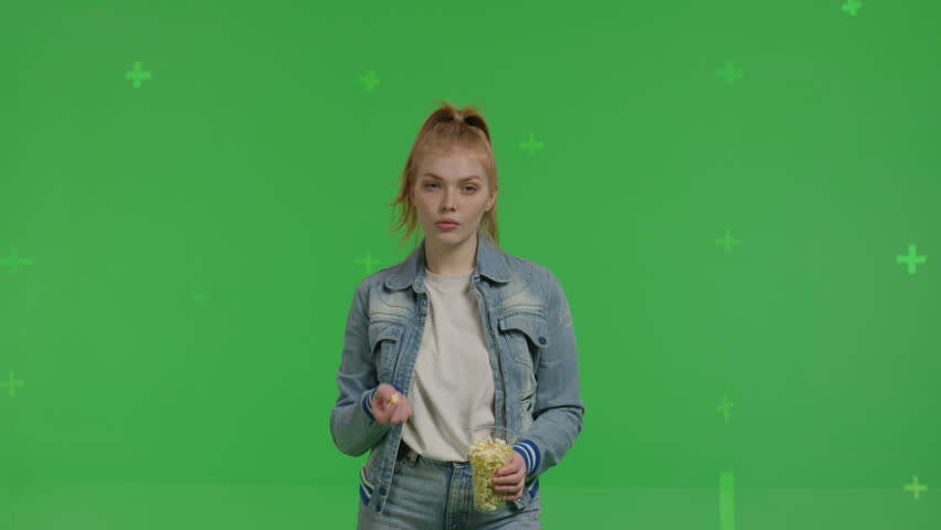 Close-up of white red-haired girl eats popcorn on a green background