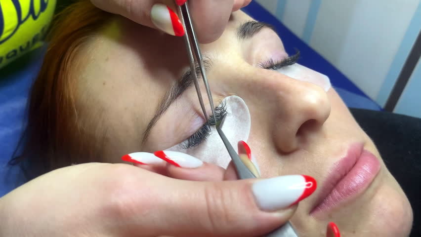 Close up eyelash extension Procedure.Eyelash extension beautician master glues takes new long artificial false eyelashes to woman client in beauty salon,dip it in black glue with tweezers,cosmetology. | Shutterstock HD Video #1101504861