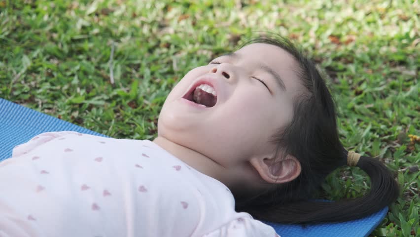 Asian cute little girl lying down using hand held fan in summer nature outdoor park.