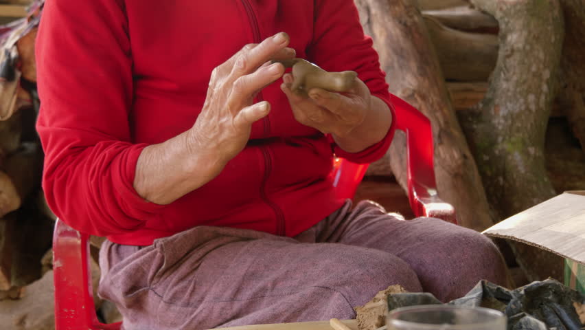 A close-up shot of an Asian woman crafting animal figures in clay for souvenir flutes in Thanh Ha, showcasing the local tourism industry.