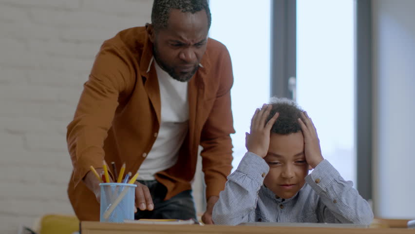 Generation gaps. Angry furious african american father scolding his little son, displeased upset boy sitting at desk and holding his head, suffering from dad's attitude, slow motion, free space Royalty-Free Stock Footage #1101507945