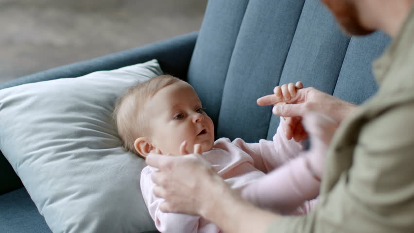 Infant entertainment. Cute little baby girl lying on sofa and clapping hands, loving unrecognizable man playing with his adorable daughter, tracking shot, slow motion, free space Royalty-Free Stock Footage #1101507969