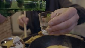 This POV video shows a soju sake bottle pouring alcohol into a shot glass in slow motion.