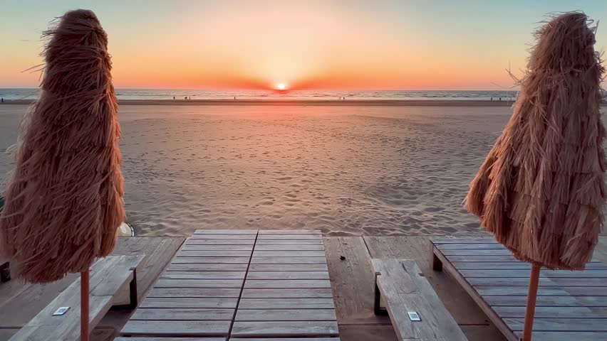 Relaxing landscape reed sun umbrellas, sandy beach and sun setting in the sea. Noordwijk, the Netherlands. High quality 4k footage