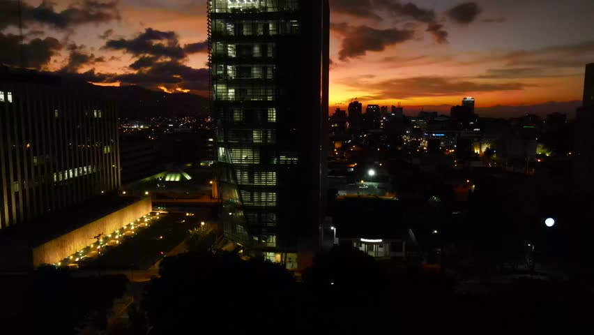 Aerial shot drone slowly lowers in front of lit up office building at sunset