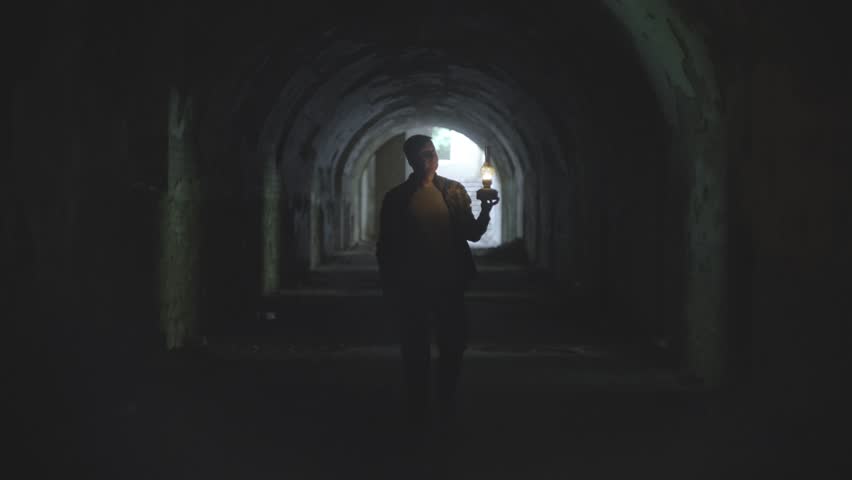 A man in a dungeon with a gas lamp. Exploring the catacombs with a torch. A mystical tunnel, a boy lights his way with a lantern. High quality 4k footage