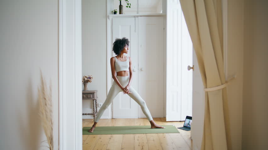 Calm lady practicing yoga at home. African american relaxed girl making pose standing carpet. Slim sportswoman stretching body at white interior. Sport trainer doing extended side angle posture alone  Royalty-Free Stock Footage #1101521625