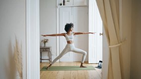 Calm lady practicing yoga at home. African american relaxed girl making pose standing carpet. Slim sportswoman stretching body at white interior. Sport trainer doing extended side angle posture alone  - Powered by Shutterstock - Get 15% off with code: PIKWIZARD15