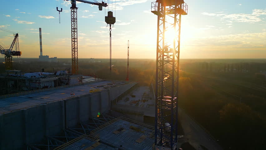 Drone point of view moving up around crane tower in construction site sunrise. Close up view of the crane tower lifting material in building site. Industry construction concept footage. Royalty-Free Stock Footage #1101528097