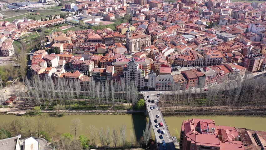Scenic drone view of modern residential areas of Aranda de Duero city on banks of Duero river on sunny spring day on background of natural rural landscape, Burgos, Spain