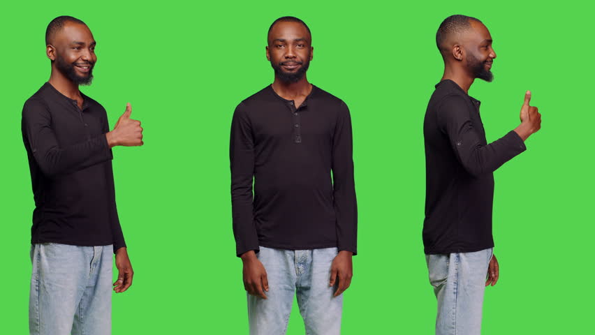 Casual person giving thumbs up on camera, showing successful gesture and agreement. Young man doing like okay symbol with approval, standing over green screen background. Optimistic adult.