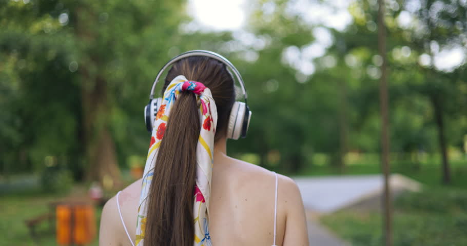 Girl listening to music in a park full of trees and greenery