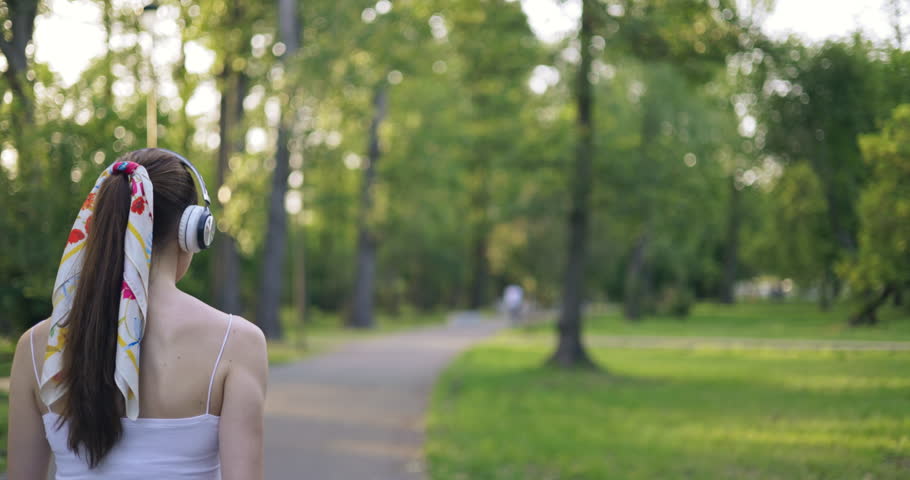 young woman in park listens to music on headphones