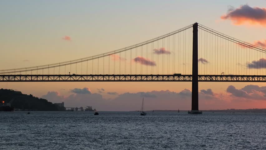 View of 25 de Abril Bridge famous tourist landmark of Lisbon connecting Lisboa and Almada on Setubal Peninsula over Tagus river on sunset. Lisbon, Portugal. Camera pan