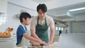 Father and cute little son are cooking and learning on tablet through videos on social media cooking together in the kitchen. Cooking concept and Family times