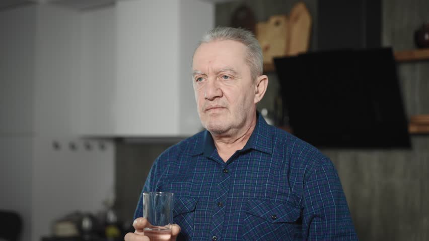 An elderly man takes medication and drinks it with a glass of water. A pensioner in his kitchen, drinking pills Royalty-Free Stock Footage #1101546603