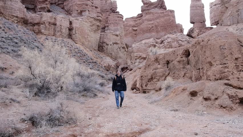 Young high man in glasses with brown backpack and fim camera walking inside canyon. High quality FullHD footage