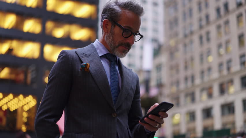 Excited mature businessman in suit and stylish eye glasses checks quotes on stock exchange using mobile phone application. Successful male enjoy Investments and cryptocurrency trading in cellphone