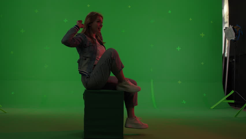 Silhouette young caucasian woman sitting on the top of a mountain or roof watching the sunset with beautiful landscape. Girl raises her hands up on Green screen background, chroma key.