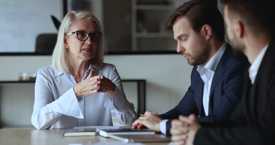Elderly and millennial colleagues, business partners engaged in formal negotiation, planning joint business and future cooperation seated at desk in company office. Meeting of client and sales manager Royalty-Free Stock Footage #1101557161