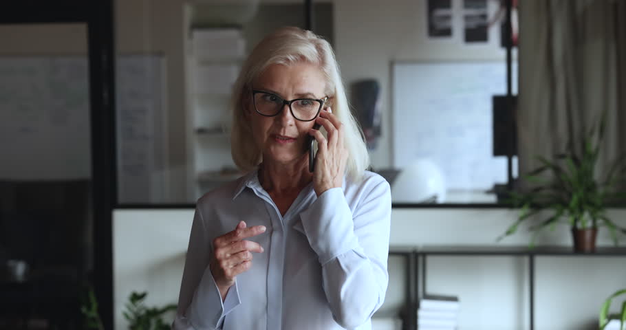 Mature businesswoman make call, having formal conversation to client by cellphone, standing at workplace, solve business remotely by phonecall, provide information, helps distantly. Mobile connection Royalty-Free Stock Footage #1101557197
