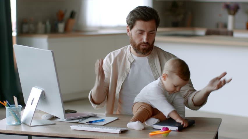 Paternity leave and remote work. Young busy man working on computer and holding his active baby daughter, suffering from lack of time at home office, tracking shot, slow motion Royalty-Free Stock Footage #1101571141