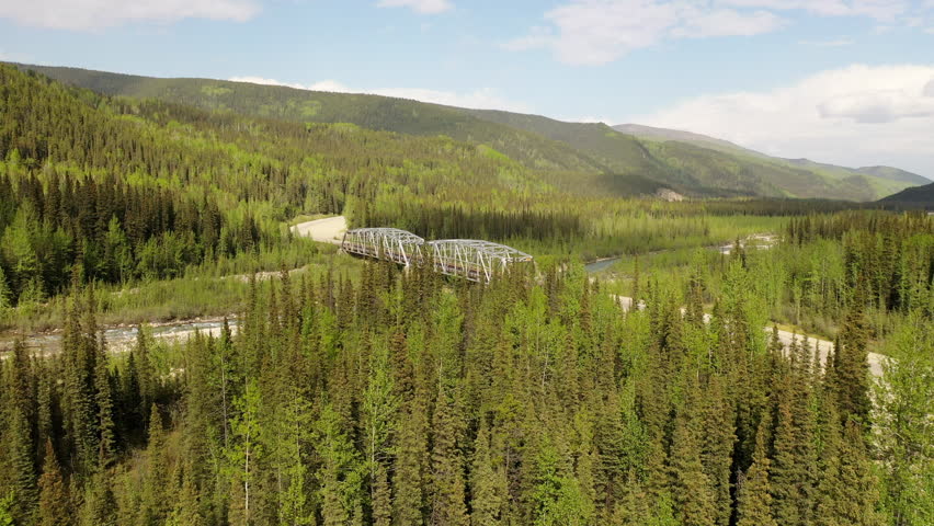 Steel bridge on the Canadian section of the Alaska Highway. Summer season, sunny day. Road, forested mountains, river Royalty-Free Stock Footage #1101572885