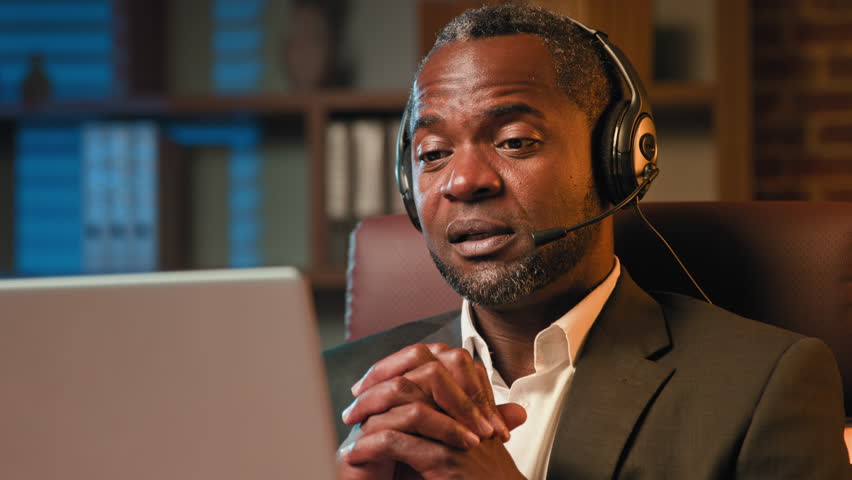 Serious african american professional mentor teacher businessman talking on video call using headset man holding online conference business negotiation explaining remote communicate webcam on laptop | Shutterstock HD Video #1101575109