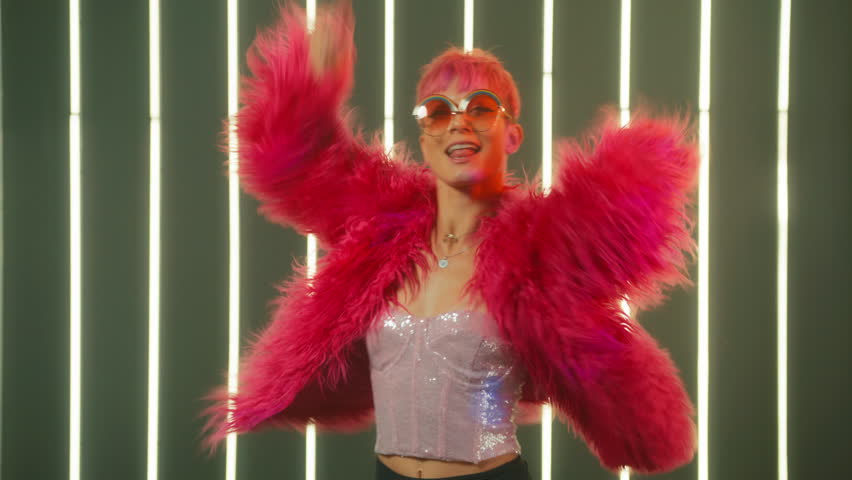 Girl in colorful clothes and pink fluffy fur coat. Happy person moving, positive emotions, ecstatic feeling. Funny young woman with original hot pink hairstyle dancing on light wall studio background