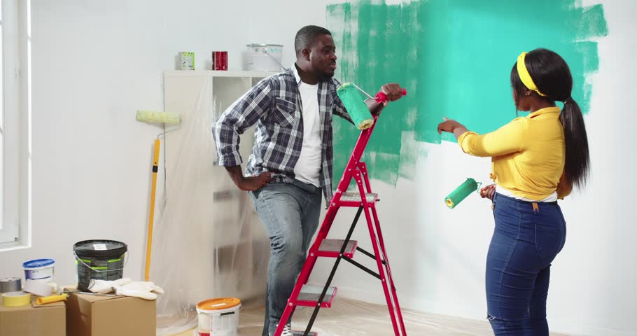Lovely couple of African American man and woman having little break after painting walls with rollers talking about renovation of apartment. Process of redesigning of flat by using green paint. Royalty-Free Stock Footage #1101593921