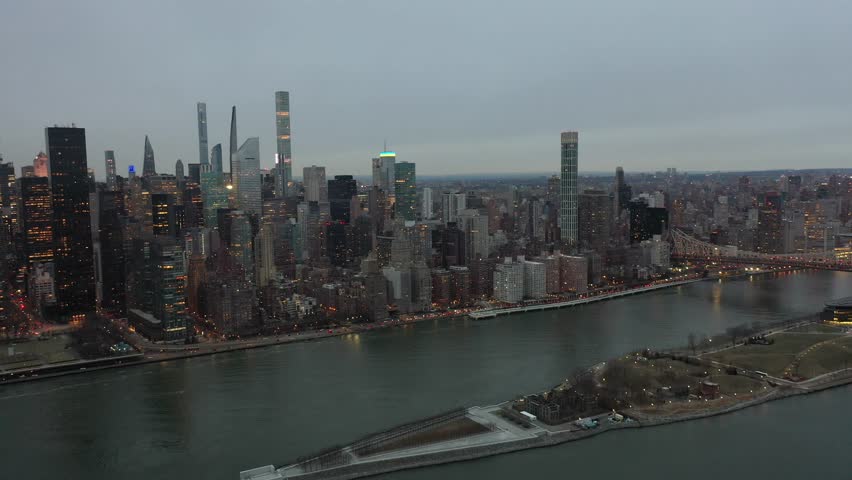 Manhattan, New York, USA - Mar. 2023 - steady aerial video view of Midtown Manhattan with Roosevelt Island, Ed Koch Queensboro Bridge across East River and illuminated traffic driving on FDR Dr.- dawn