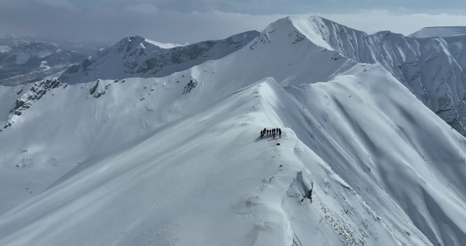Cinematic Aerial Epic scene of group of skiers and snowboarders on top of a mountain. Winter at the summit peak or top with a group of freeride or backcountry skiers.