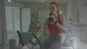 Animation of white spots over caucasian woman exercising, using stationary bike at home. Global fitness and connections concept digitally generated video.