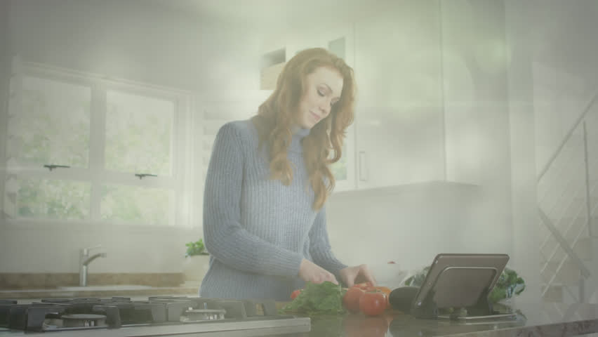 Animation of light spots over caucasian woman chopping vegetables and using tablet in kitchen. Lifestyle, cooking and nutrition concept digitally generated video.