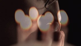 Composite video of burning candles against close up of a caucasian woman praying. Prayers and religion concept