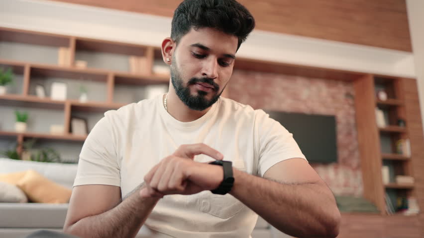Active arabic bearded man setting heart-rate watch while having rest after fitness training indoors. Physically active male in sportswear checking results of home workout plan using fitness tracker. Royalty-Free Stock Footage #1101603147