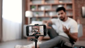 Confident sports coach pointing finger at camera and motivating followers to regular physical exercise and active lifestyle. Selective focus of smartphone on tripod filming video content for sharing.