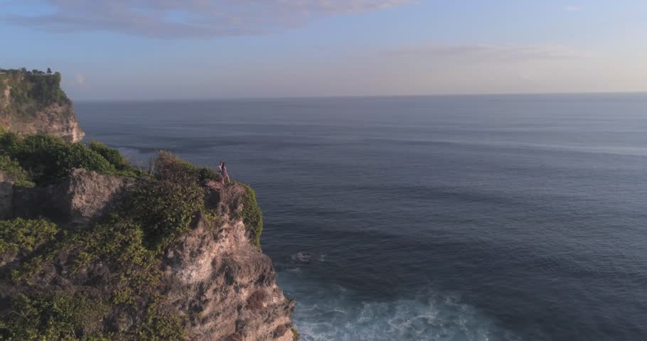 Loving couple of people is staying on the edge of the cliff above ocean on beautiful sunset. Romantic atmosphere, aerial view, drone shot. Uluwatu area in Bali, Indonesia | Shutterstock HD Video #1101605521