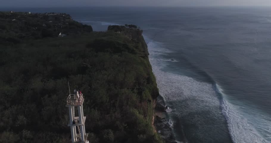 Couple is staying on the top of white abandoned lighthouse on a cliff above ocean on beautiful sunset. Romantic place, chilling, relaxing atmosphere, love concept. Aerial view, drone shot | Shutterstock HD Video #1101605527