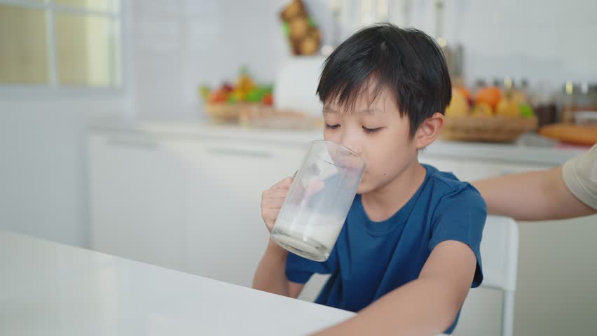 Happy Asian little cute kid boy holding a cup of milk in kitchen enjoy drinking milk at home Royalty-Free Stock Footage #1101605611