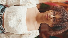 VERTICAL VIDEO: Closeup portrait of young woman in glasses stands next to a flower shop and looks at the camera and smiling. Girl posing on camera