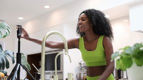 A Young African Woman Recording a Video Tutorial on How to Prepare Matcha Tea in Her Kitchen. YouTuber Recording  With Phone A Tutorial In Sportive Outfit