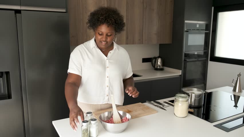 Young cuban woman adding salt, parsley and mixing raw minced beef and garlic to prepare cuban style stuffed potatoes.