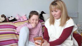A girl of 7 years old and a young woman are watching a video on a smartphone. The child has a cold, coughs a lot, a cold virus.