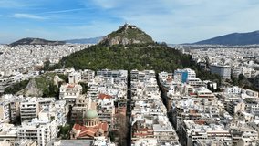 Aerial drone cinematic video of Athens cityscape and iconic chapel of Saint George on top of Lycabettus hill with beautiful deep blue sky, Athens, Attica, Greece