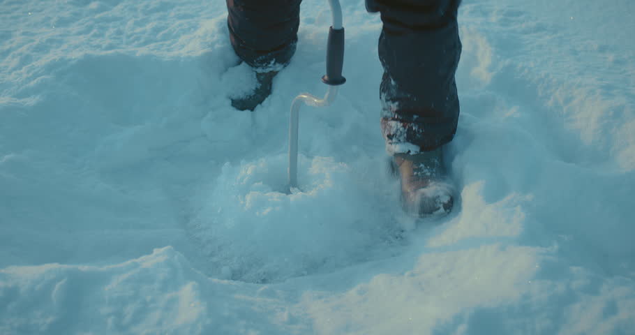 man is making ice hole in frozen river, closeup view of fisher shoes and ice drill, 4K, Prores