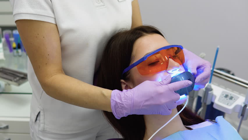 Teeth whitening procedure with ultraviolet light UV lamp. Close-up portrait of a female patient at dentist in the clinic | Shutterstock HD Video #1101617109