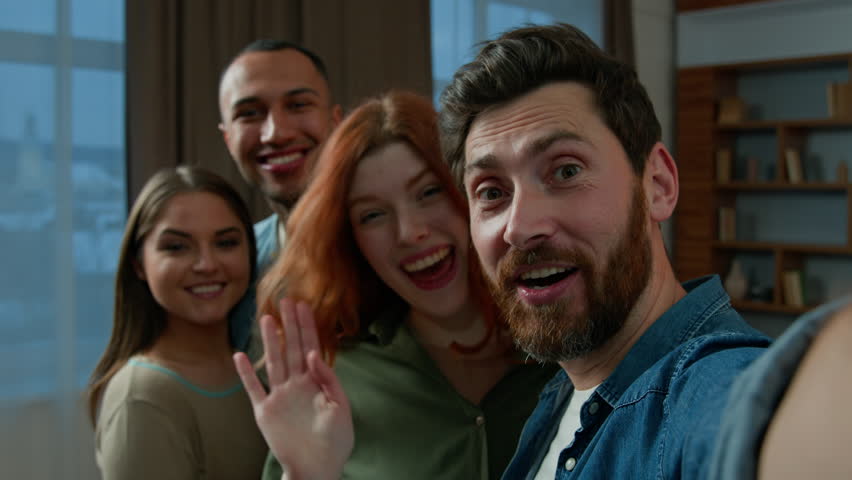 Bearded man blogger hold mobile phone invite friends colleagues group photo diverse multiracial men women looking at smartphone camera smiling laughing make funny selfie record video blog webcam view