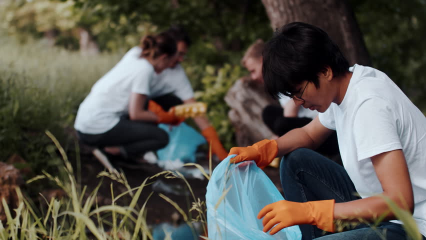 Young asian ecological volunteer as a part of the group cleaning debris by hand in forest and looking confident. Caring persons thinking about the future and voluntarily fights against environmental | Shutterstock HD Video #1101618227