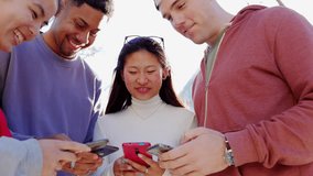 Happy young group of multiracial friends having fun together using mobile phone in the street. Millennial teenage people watching funny videos on smartphone enjoying social media content. 
